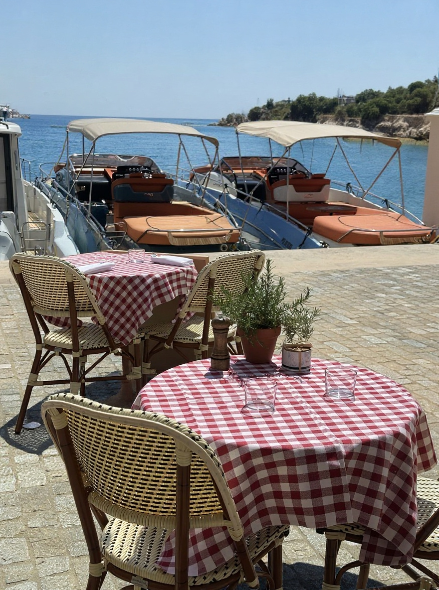 La terrasse de Chez Manou sur le port de Saint-Jean-Cap-Ferrat — nappes vichy rouges, chaises en rotin, le port et les voiliers